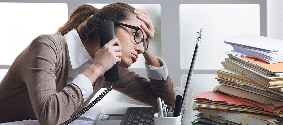 Woman sitting at a desk on the phone staring at computer and looking stressed out